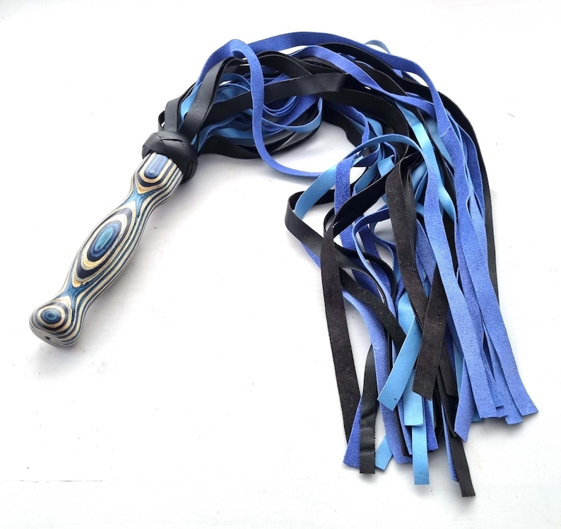 May include: A handcrafted flogger with a wooden handle featuring blue and white swirls. The flogger's falls are a mix of black, light blue, and dark blue leather strips, creating a striking contrast. The handle is wrapped in black leather.