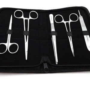 Può includere: Una custodia nera con cerniera contenente un set di quattro strumenti chirurgici: due paia di pinze, un paio di forbici e un bisturi.