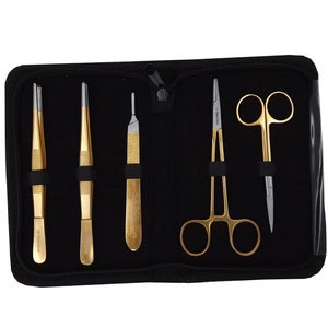 May include: A black zippered case containing a set of five gold-toned surgical instruments. The instruments include two pairs of tweezers, a scalpel, and a pair of scissors.