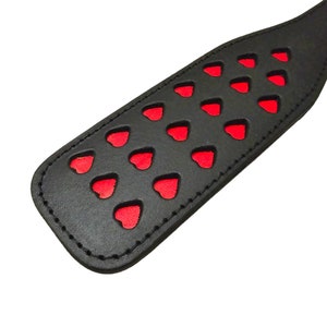 May include: Black leather paddle with red heart cutouts.