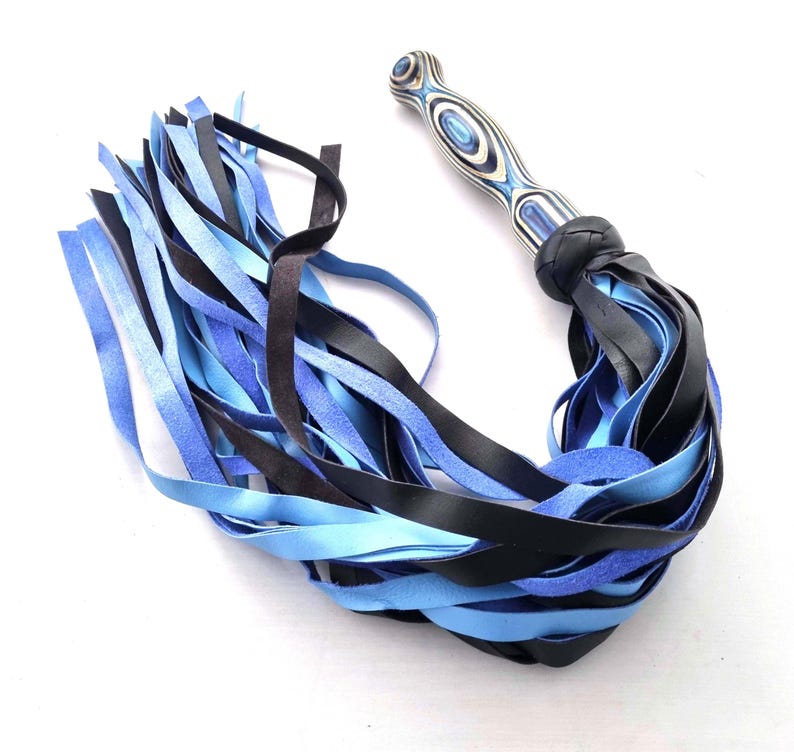 May include: A flogger with a wooden handle featuring a blue and white swirl pattern. The flogger's fall is composed of black and shades of blue leather strips, knotted at the base of the handle.