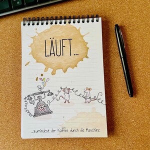 Könnte beinhalten: Spiralgebundenes Notizbuch mit Kaffeefleck-Design und dem Wort "LÄUFT..." auf der Vorderseite. Das Notizbuch zeigt eine skurrile Illustration von Mäusen und einem Vintage-Telefon. Ein schwarzer Stift liegt neben dem Notizbuch.