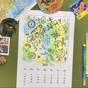 May include: A July calendar page with the word "GEOGRAPHY" and related illustrations. The page is surrounded by colorful markers, magnets, and a map. The calendar includes dates for the month of July.