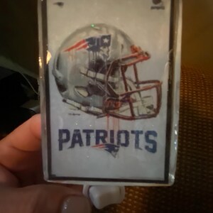 May include: A white night light with a clear plastic cover featuring a football helmet and the word "Patriots".