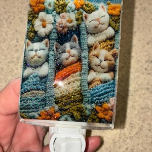 Puede incluir: Una luz de noche rectangular con cinco gatos sonrientes en mantas acogedoras. Los gatos son blancos, grises y naranjas, rodeados de flores en tonos naranja, blanco y verde. El fondo es azul texturizado con brillos.