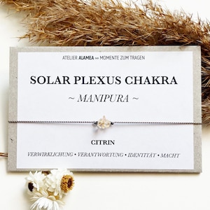Könnte beinhalten: Ein Citrin-Kristallarmband auf einer Karte mit dem Text "SOLAR PLEXUS CHAKRA ~ MANIPURA ~ CITRIN". Die Karte enthält auch die Wörter "VERWIRKLICHUNG • VERANTWORTUNG • IDENTITÄT • MACHT". Das Armband ist an einem grauen Kordel befestigt.