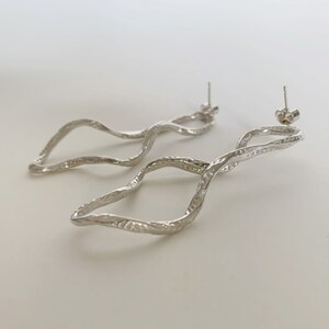 May include: A pair of silver earrings with a wavy, organic design. The earrings are made of a textured metal and have a post back.