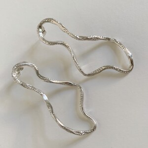 May include: A pair of silver earrings with a wavy, organic shape. The earrings are textured and have a polished finish.