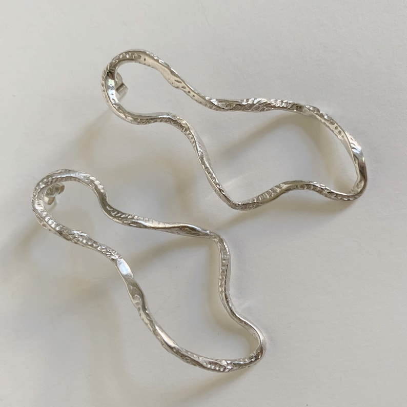 May include: A pair of silver earrings with a wavy, organic shape. The earrings are textured and have a polished finish.