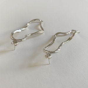 May include: A pair of silver earrings with a unique, wavy, organic shape. The earrings are made of a textured metal and have a post back.