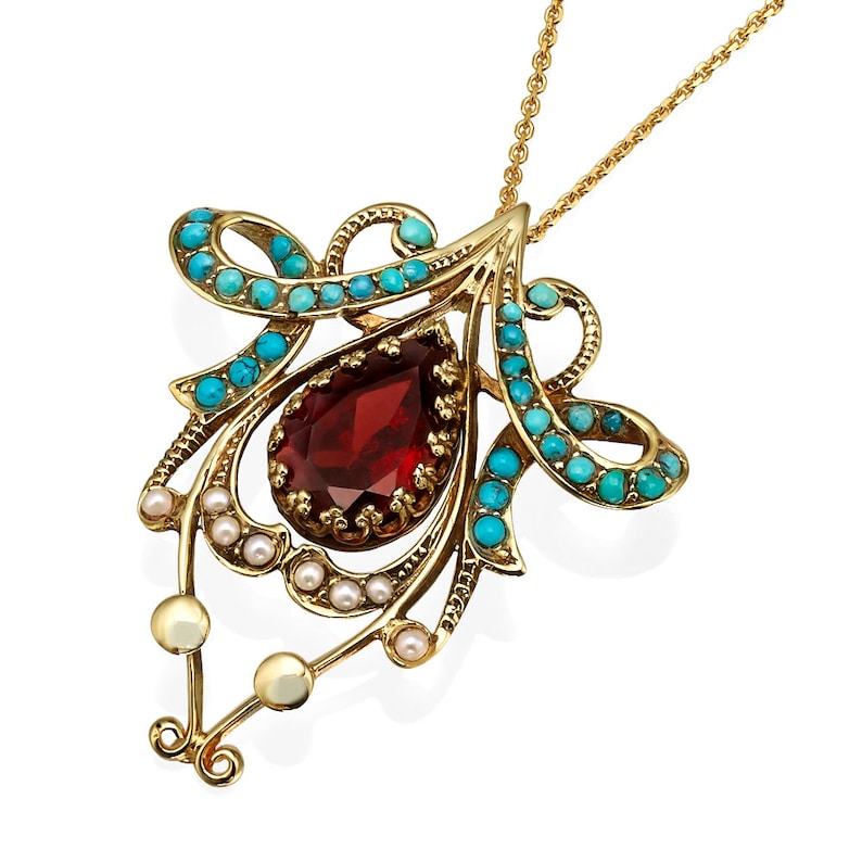 May include: A gold-toned pendant necklace featuring a teardrop-shaped, deep red gemstone at its center. The pendant is adorned with small, round turquoise stones and tiny pearls. The necklace has a delicate chain.