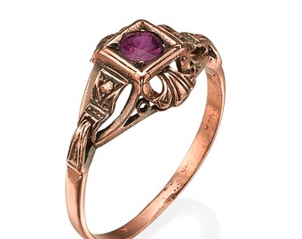 May include: A vintage-style ring with a square setting. The ring features a vibrant, round, magenta gemstone. The band and setting are a warm, copper color, with intricate filigree and geometric details. A classic piece of jewelry.