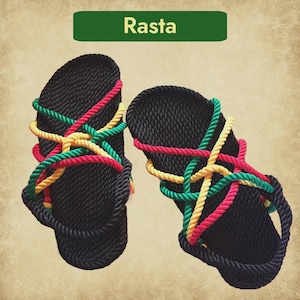 Può includere: Un paio di sandali in corda neri con dettagli in corda rossa, gialla e verde. I sandali hanno una suola strutturata e la parola "Rasta" è visualizzata su uno striscione verde. Calzature estive.