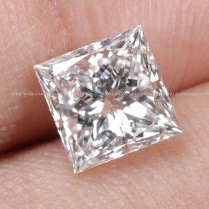 Peut inclure: Un diamant clair de taille carrée avec de multiples facettes, tenu dans une main. Le diamant reflète la lumière, mettant en valeur son éclat. La pierre précieuse est une taille princesse, un choix populaire pour les bagues de fiançailles et les bijoux fins.