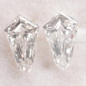 May include: Two clear, kite-shaped gemstones with multiple facets, reflecting light. The gems are set against a soft, white background. The gemstones are likely diamonds, showcasing a unique cut and brilliance.