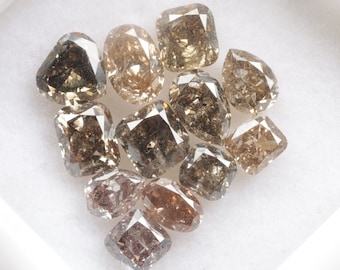 May include: A collection of brown, gray, and champagne-colored diamonds in a white box. The diamonds are all cut in a square shape.