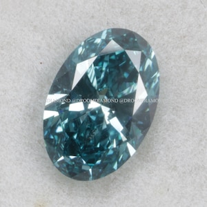 May include: An oval-shaped, teal-colored gemstone with multiple facets. The gem has a brilliant cut, reflecting light and creating a sparkling effect. The stone is set against a neutral background.