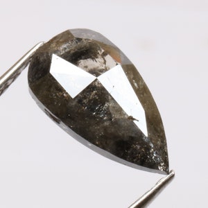 Op de afbeelding: Een peervormige, donkergrijze diamant met een facetgeslepen vorm. De diamant heeft veel insluitsels en zit in een pincet.