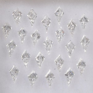 Puede incluir: Una colección de veintiún diamantes en forma de cometa, cada uno con una superficie facetada, dispuestos sobre un fondo blanco. Los diamantes son claros y brillantes, reflejando la luz. La forma de cometa es un diseño único y elegante.