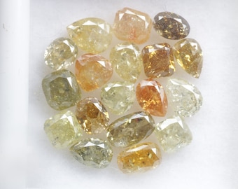 May include: A collection of 17 rough cut diamonds in various shades of yellow, green, and brown. The diamonds are displayed in a white box.