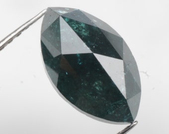May include: A marquise-cut gemstone in a dark teal hue, held by metal tweezers against a white backdrop. The gem features multiple facets that reflect light, producing a sparkling effect. The shape is elongated and pointed at both ends.