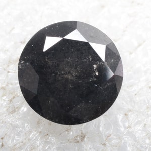 May include: A black round gemstone with a faceted cut. The gemstone has a dark, opaque appearance with a slight sheen.