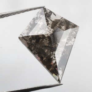 K&ouml;nnte beinhalten: Ein klarer, facettierter, quadratischer Diamant mit schwarzen Einschl&uuml;ssen. Der Diamant wird von einer Pinzette gehalten.