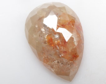 May include: A faceted, pear-shaped gemstone with a light brown hue and internal orange and red inclusions. The gem has a polished surface with multiple facets, reflecting light. The overall shape is elongated with a pointed base.