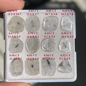 Op de afbeelding: Een witte lade met 12 heldere, gefacetteerde edelstenen. Elke edelsteen is gelabeld met zijn karaatgewicht en afmetingen in millimeters. De lade is gemaakt van plastic en heeft een witte achtergrond.