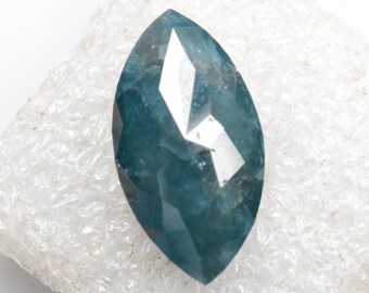 May include: A dark blue marquise-shaped gemstone with a faceted cut. The gemstone is set on a white background.