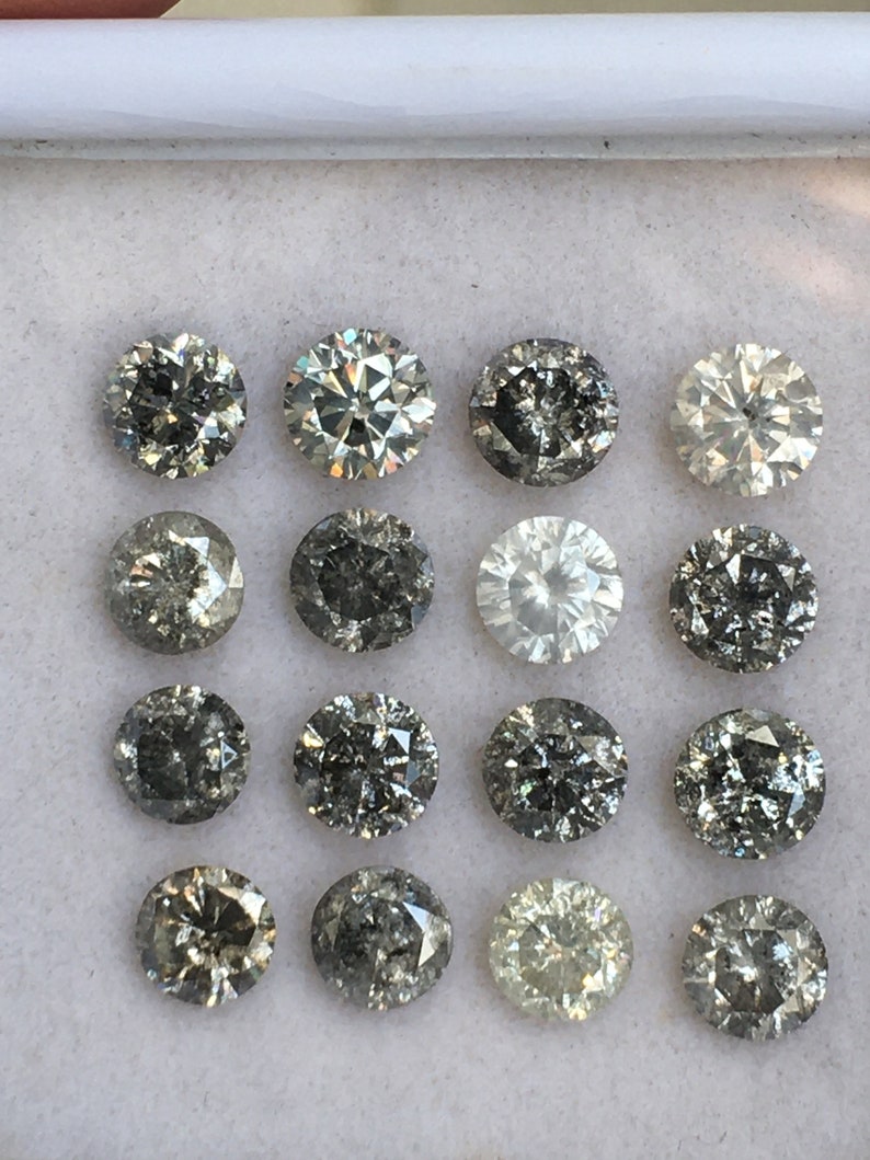 May include: A collection of 16 round, faceted, grey diamonds in a white box. The diamonds are arranged in four rows of four.