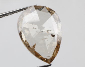 May include: A pear-shaped, light brown diamond with a faceted cut. The diamond is held by tweezers against a white background.