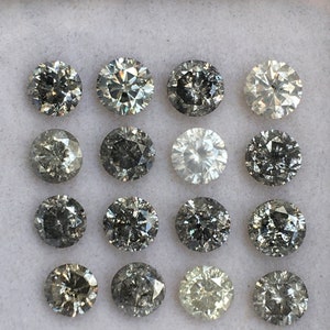 May include: A collection of 16 round, faceted, grey diamonds in a white box. The diamonds are arranged in four rows of four.