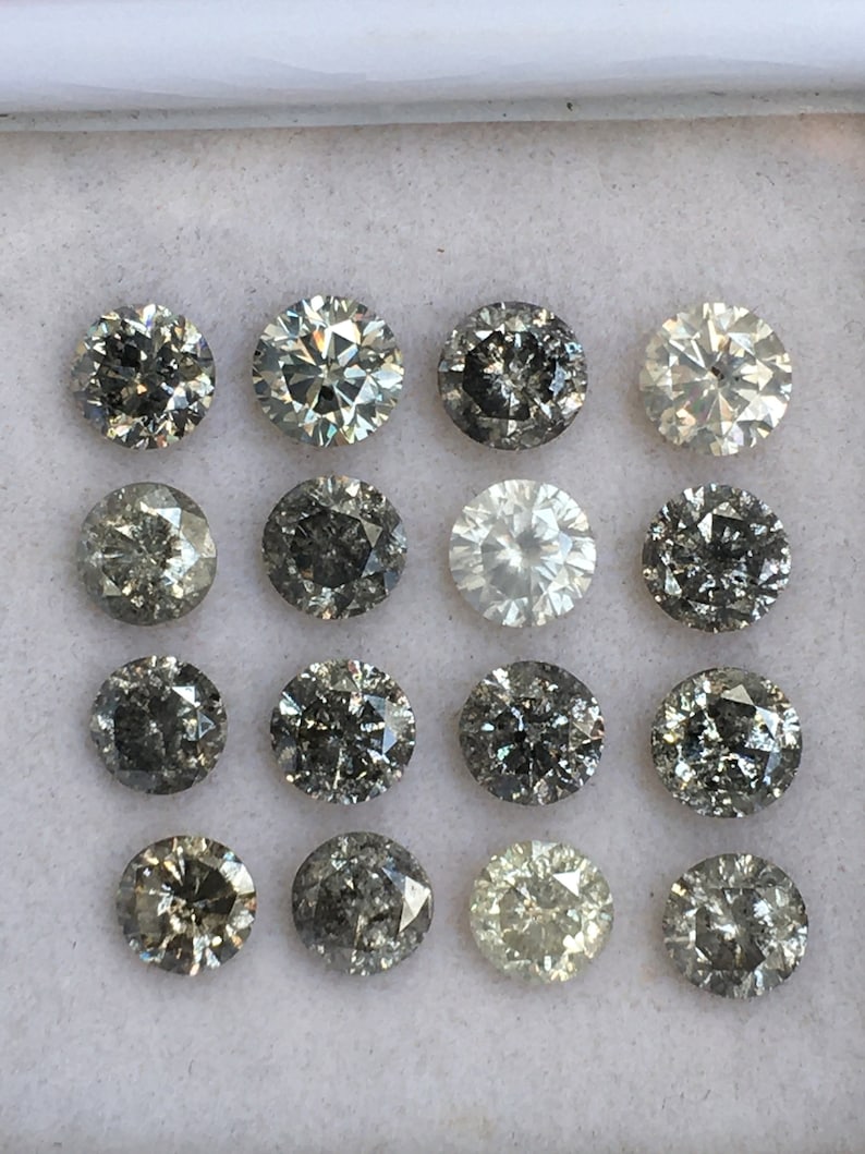 May include: A collection of 16 round, faceted, grey diamonds in a white box. The diamonds are arranged in four rows of four.