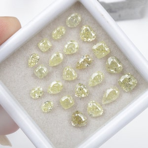 May include: A collection of 20 loose yellow diamonds in various shapes and sizes, displayed in a white box.