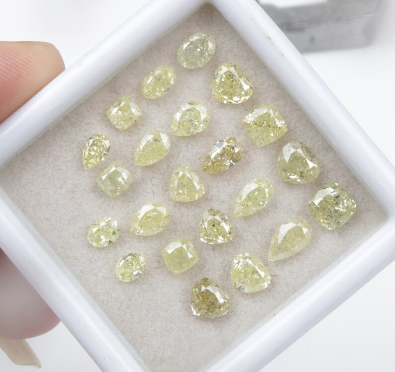 May include: A collection of 20 loose yellow diamonds in various shapes and sizes, displayed in a white box.