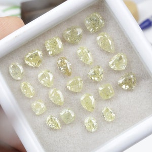 May include: A collection of 20 loose yellow diamonds in a white box. The diamonds are various shapes and sizes.