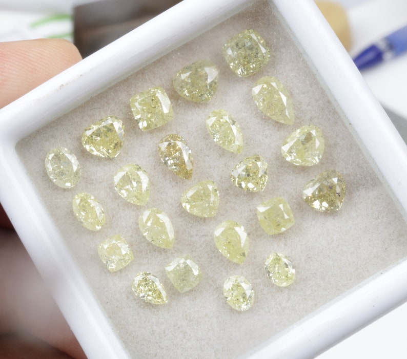 May include: A collection of 20 loose yellow diamonds in a white box. The diamonds are various shapes and sizes.
