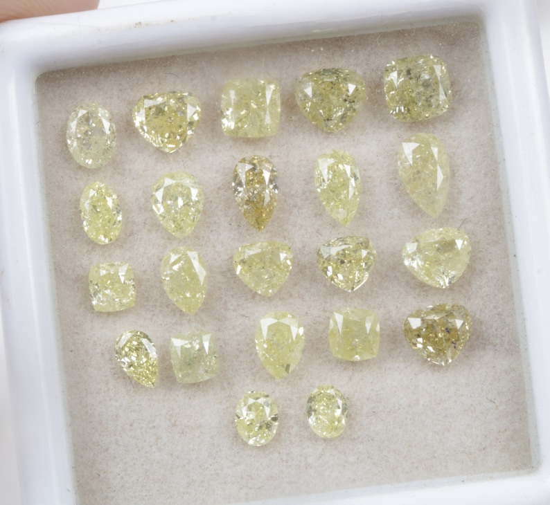 May include: A collection of 20 loose yellow diamonds of various shapes and sizes, displayed in a white tray.