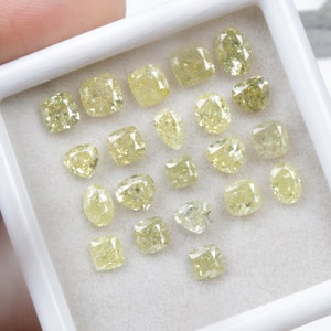 May include: A collection of yellow diamonds of various shapes and sizes displayed in a white box. The diamonds are arranged in a random pattern.
