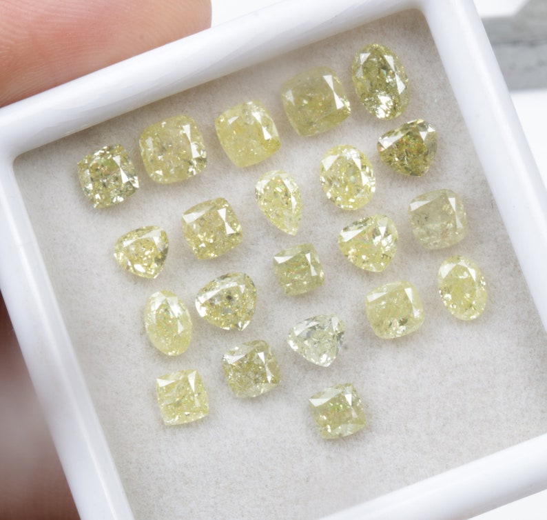 May include: A collection of yellow diamonds of various shapes and sizes displayed in a white box. The diamonds are arranged in a random pattern.