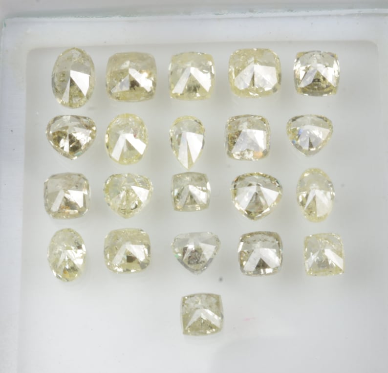 May include: Assortment of 21 loose, faceted, light yellow diamonds in a white tray. The diamonds are various shapes and sizes.