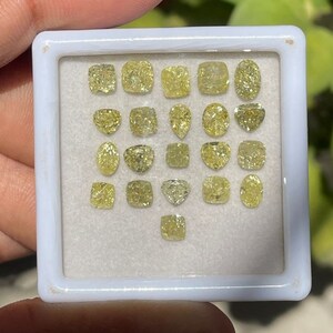 May include: A white tray containing 20 yellow gemstones of various shapes and sizes. The gemstones are arranged in rows and columns.