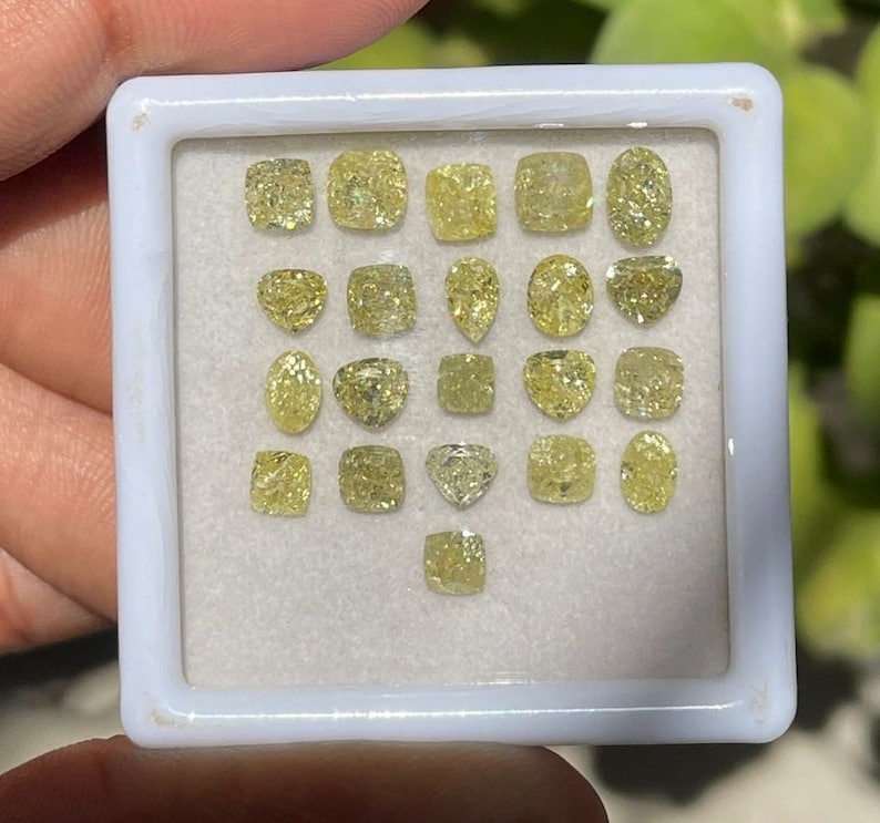 May include: A white tray containing 20 yellow gemstones of various shapes and sizes. The gemstones are arranged in rows and columns.
