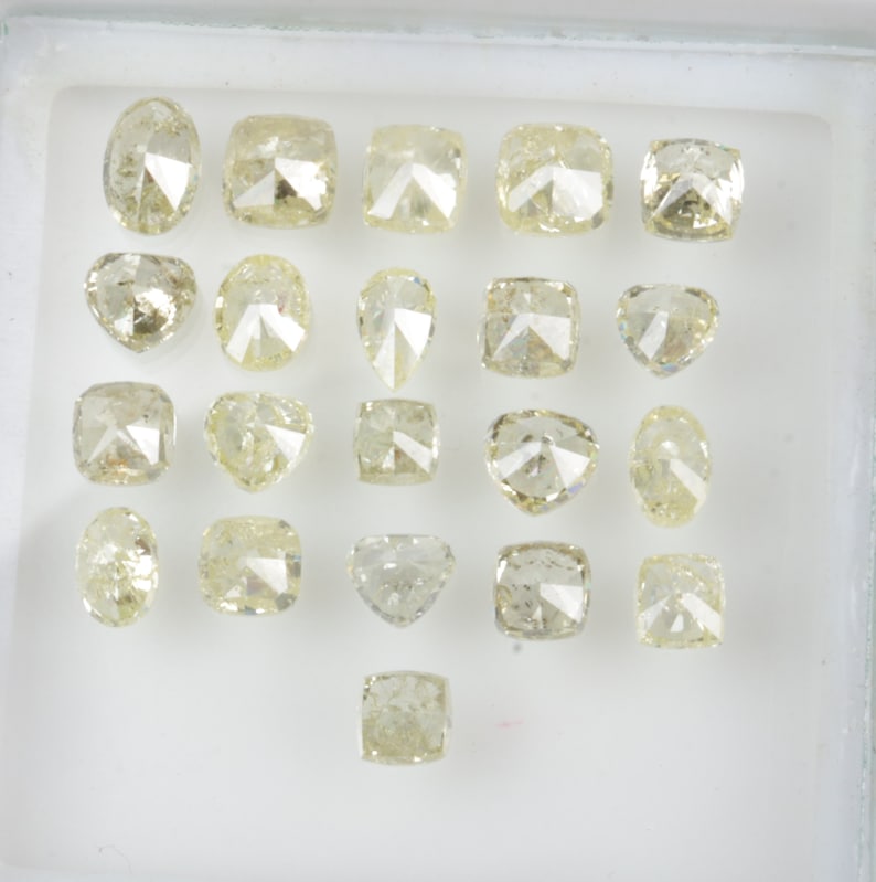 May include: A collection of 18 loose, faceted, pale yellow diamonds in various shapes and sizes, displayed in a white tray.