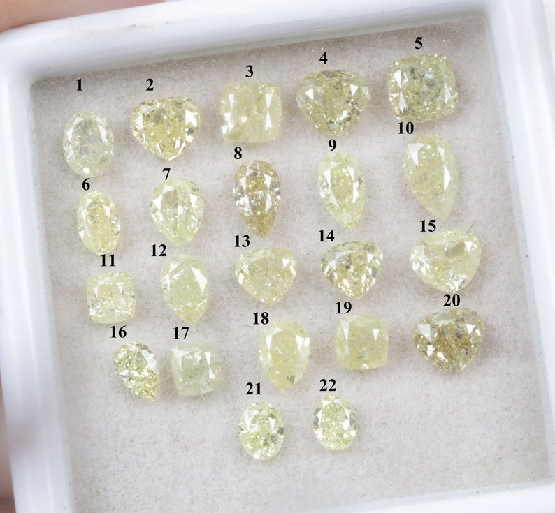 May include: Twenty-two loose yellow diamonds of various shapes and sizes, numbered 1 through 22, displayed in a white tray.