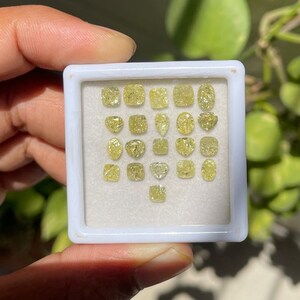May include: A white box with a clear lid containing a collection of 25 loose yellow diamonds of various shapes and sizes.