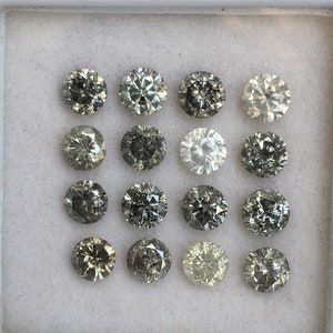 May include: A collection of 15 round, gray diamonds in a white box. The diamonds are arranged in three rows of five.