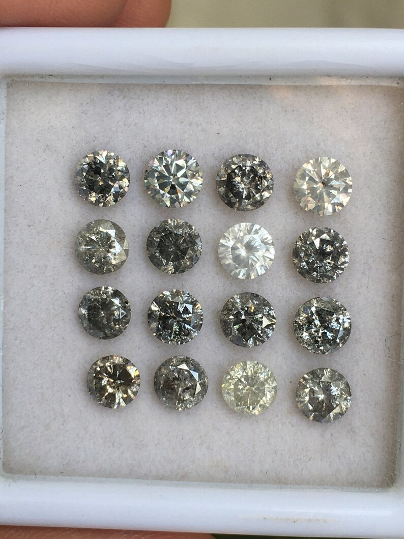 May include: A collection of 15 round, gray diamonds in a white box. The diamonds are arranged in three rows of five.