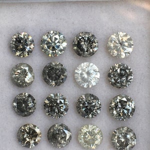 May include: A collection of 16 round, faceted, gray diamonds in a white box. The diamonds are arranged in four rows of four.